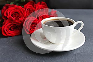 Black coffee in a white Cup with a saucer on the table, a bouquet of red roses.