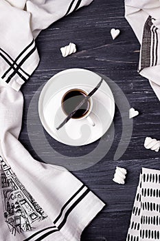 Black coffee in a white cup, vanilla bean, marshmallow and black-white kitchen towel on a dark background