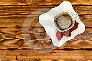 Black coffee in whute cup with strawberry, cinnamon and spices on a wooden red table