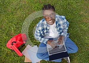 Black college student guy typing on laptop PC sits outside