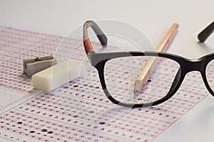 Black color glasses,wooden pencil and rubber on filled exam sheet