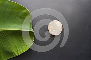 Black Color Paper Texture Background With Banana Leaves And Round Wood. Creative idea concept. Minimalism. Top view. Banana Leaf