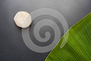 Black Color Paper Texture Background With Banana Leaves And Round Wood. Creative idea concept. Minimalism. Top view. Banana Leaf