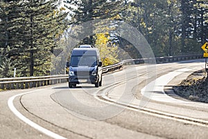 Black compact commercial mini van running on the winding road with autumn forest on the side photo