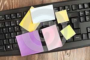 A black computer keyboard with colored paper notes on a wooden desk