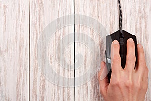 Black computer mouse with a hand on a white wooden background with copy space for your text. Top view