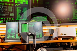 Black condenser microphone with green LED light, hacker coding interface on monitors, modern dark tech workspace setup
