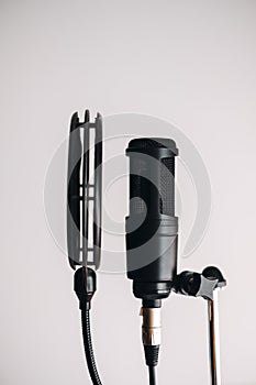 Black condenser microphone on stand with pop filter isolated on gray background