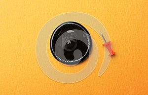 Black condom and pin on orange background