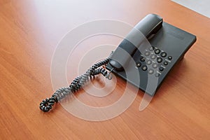Black corded telephone with buttons on a brown office table