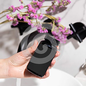 Black cosmetic jar bottle in hand with yellow capsules on a light background in the bathroom with mint and purple