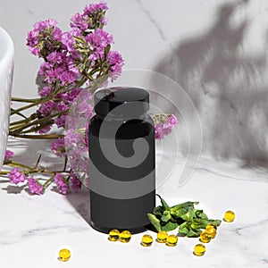 Black cosmetic jar bottle with yellow capsules on a light background in the bathroom with mint and purple flowers