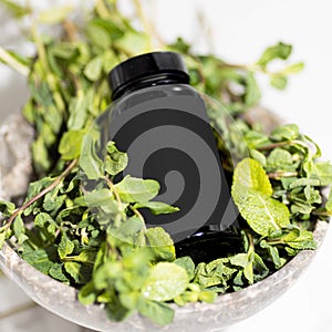 Black cosmetic jar bottle with yellow capsules on a light background in the bathroom with mint and purple flowers