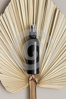 Black cosmetic spray bottle mockup with a palm leaf on the beige table