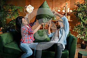 Black couple having fun on sofa, pillow fight