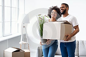 Black Couple Holding Packed Boxes Moving New House Standing Indoors