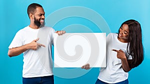 Black couple holding and pointing at blank white advertising board