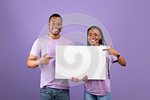 Black couple holding and pointing at blank white advertising placard