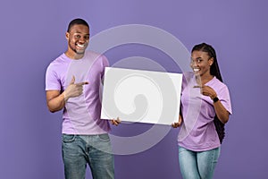 Black couple holding and pointing at blank white advertising placard