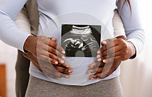 Black couple holding ultrasound image in front of woman belly