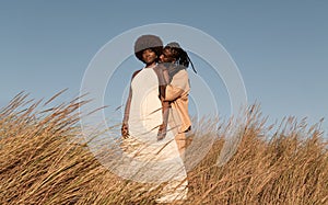 Black couple hugging in field against blue sky