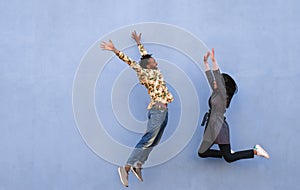 Black couple jumping outdoor with blue wall in background - Crazy happy african friends having fun together - Youth, friendship