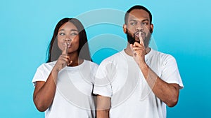 Black couple puting finger on lips, making hush sign