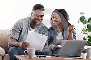 Black couple reading financial documentation at home while planning family budget