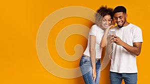 Black couple sharing headphones, choosing music on mobile application