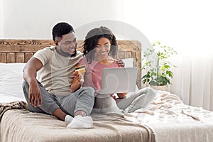 Black couple shopaholics making purchases online, using laptop