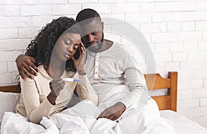 Black couple sitting on bed with negative pregnancy test result
