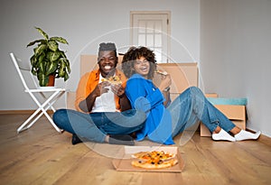 Black couple sitting on floor and eating pizza, resting after moving home