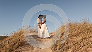 Black couple standing closely on sandy field with dry grass plants in daylight