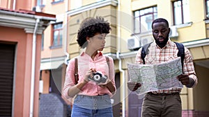 Black couple of tourists with map and photo camera, choosing direction, travel
