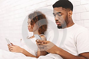 Black couple using cellphones in bed, ignoring each other