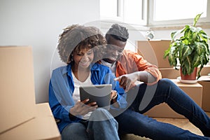 Black couple using digital tablet while sitting on floor in new apartment