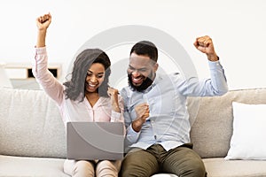 Black couple using laptop celebrating success shaking fists