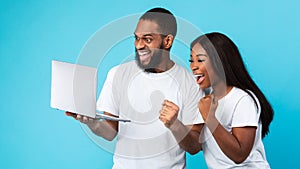 Black couple using laptop celebrating success shaking fists