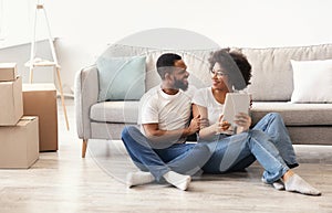 Black Couple Using Tablet Sitting Indoors, Among Moving Boxes