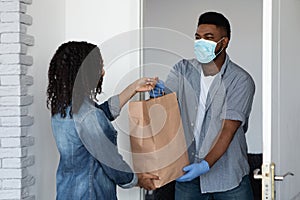 Black courier guy in medical mask delivering grocery order to woman