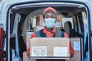 Black courier man delivering package in front of cargo truck wearing safety mask - Focus on face