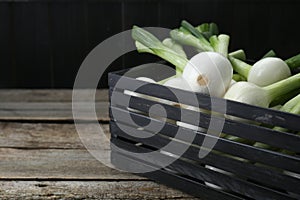 Black crate with green spring onions on wooden table, closeup. Space for text