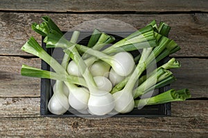 Black crate with green spring onions on wooden table, top view