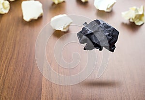 Black Crumpled paper ball floating around white paper ball on wood table, Business concept