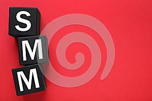Black cubes with abbreviation SMM Social media marketing on red background, flat lay. Space for text