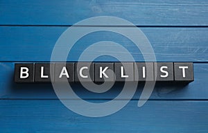 Black cubes with word Blacklist on blue wooden table, flat lay