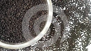 Black cumin seeds or black caraway seeds in a glass bowl rotating top left corner with spices spilled around it, white background