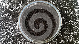 Black cumin seeds or black caraway seeds in a glass bowl spices spilled around it, rotating on white background, top view