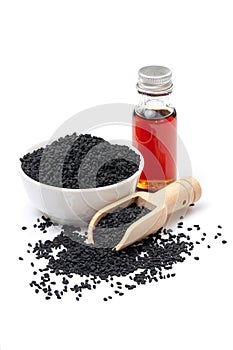 Black cumin seeds in bowl and essential oil in glass bottle.