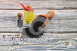 Black cumin seeds and essential oil with bowl and wooden shovel or spoon.